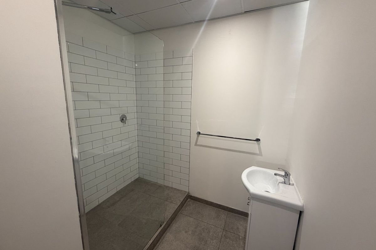 A clean, modern bathroom featuring a walk-in shower with subway tiling, a glass screen, and a pedestal sink.