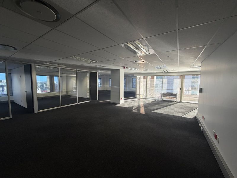 Spacious, open-plan commercial office space featuring glass partitioning, suspended ceilings with recessed lighting, and large windows providing ample natural light.