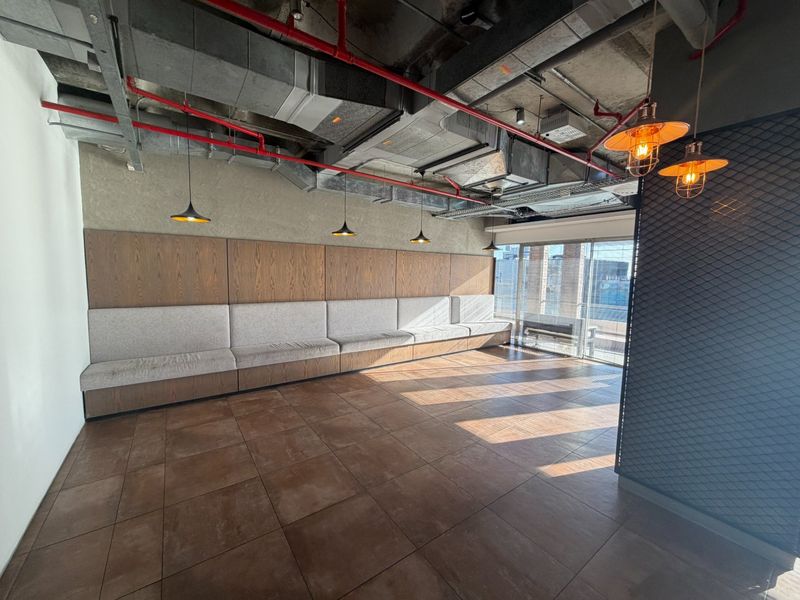 Modern industrial-style office space featuring exposed ceilings, tiled flooring, built-in bench seating, and large sliding glass doors providing natural light.