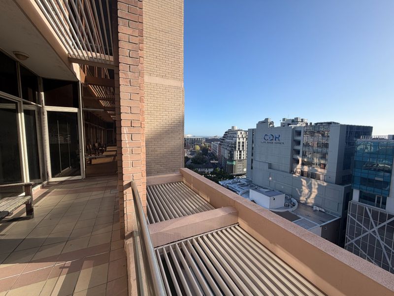 A spacious elevated balcony featuring tiled flooring, brick exterior walls, and metal louvred sun shading, offering an expansive urban view.