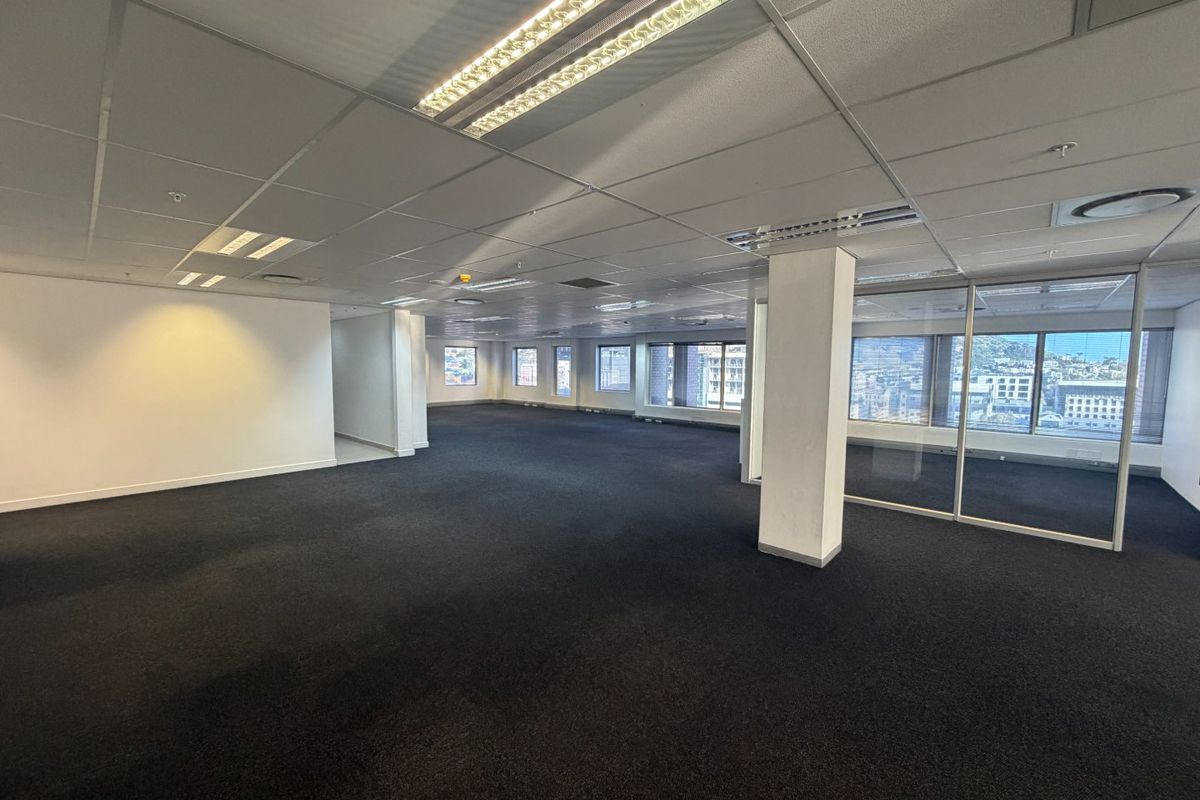 Spacious open-plan commercial office area featuring suspended ceilings, recessed lighting, dark carpeting, and glass partitioning with expansive city views.