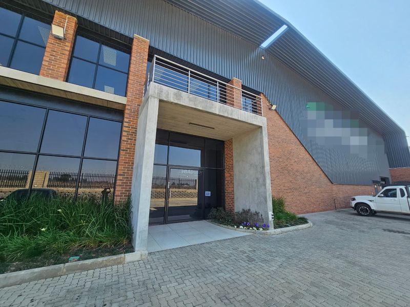 Modern industrial building facade featuring a combination of brick and metal cladding, a prominent concrete entrance canopy, and a second-floor balcony.