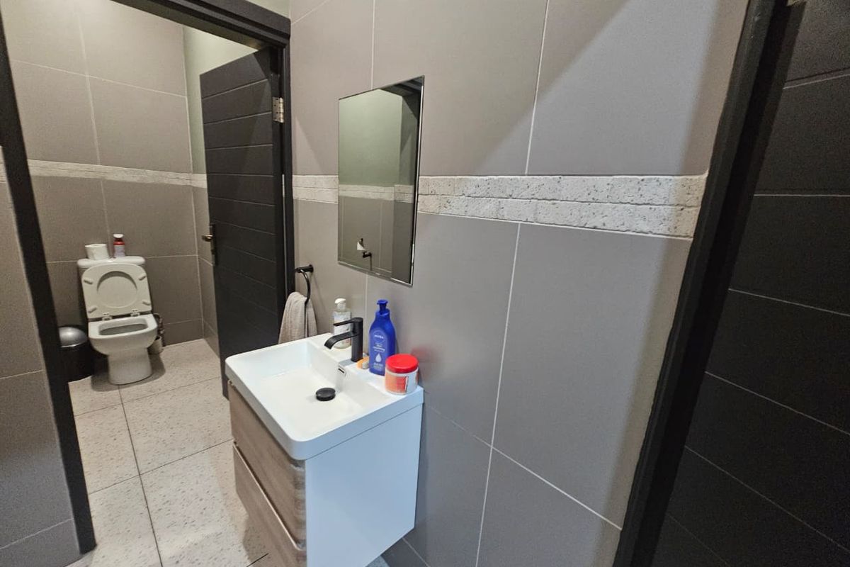 Modern bathroom featuring grey tiled walls, a wall-mounted vanity with a ceramic basin, black fixtures, and a separate toilet area.