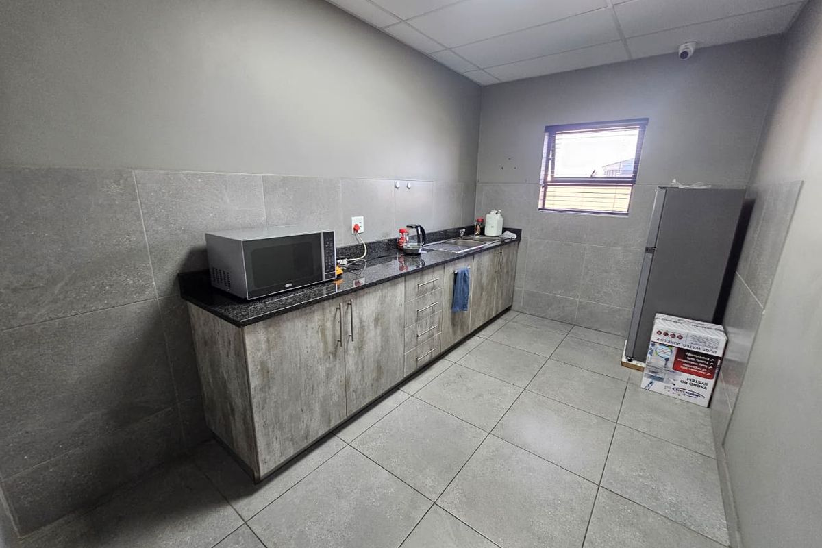 A functional industrial kitchen area featuring granite countertops, modern cabinetry, tiled splashbacks, and durable floor tiles.