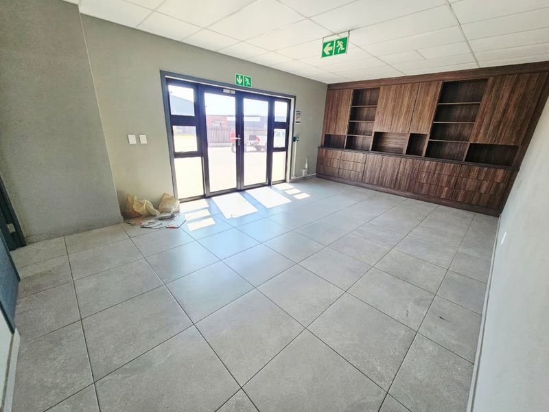 A bright, empty office space featuring large-format floor tiles, a suspended ceiling, and extensive built-in wooden cabinetry for storage.