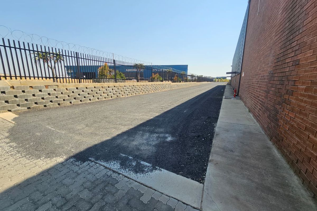 Exterior view of an industrial property featuring a paved driveway, brick facade, and secure perimeter fencing with razor wire.