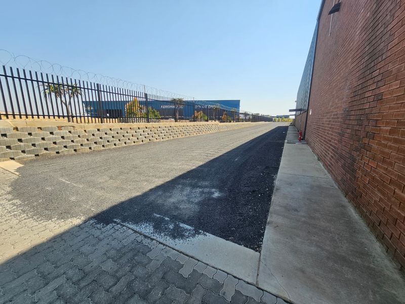Exterior view of an industrial property featuring a paved driveway, brick facade, and secure perimeter fencing with razor wire.