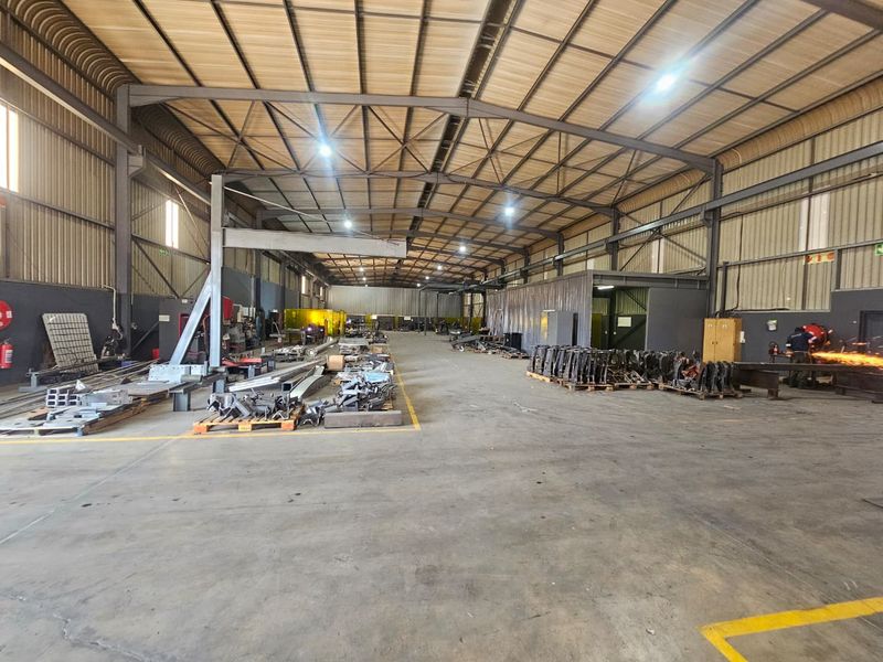 Spacious industrial warehouse featuring a steel portal frame, high-bay lighting, and durable concrete flooring, suitable for manufacturing or storage operations.