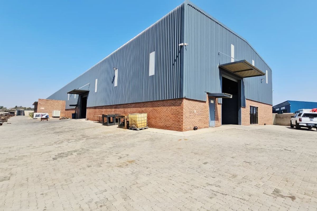 Industrial warehouse facility featuring a combination of brick and corrugated metal cladding, multiple roller shutter access points, and a spacious paved yard area.