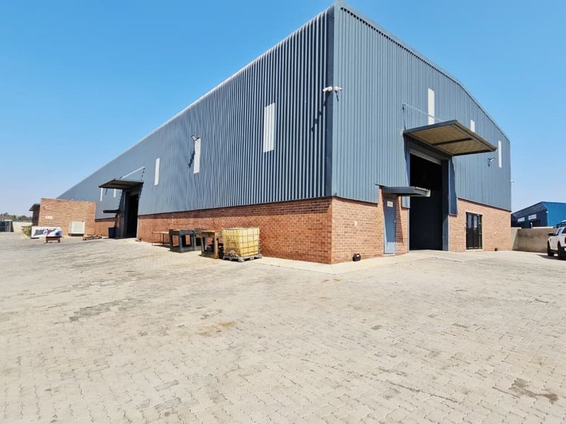 Industrial warehouse facility featuring a combination of brick and corrugated metal cladding, multiple roller shutter access points, and a spacious paved yard area.