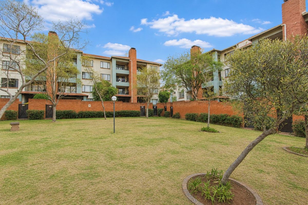 A view of the apartment complex rear facade featuring a well-maintained communal garden and brick boundary wall.