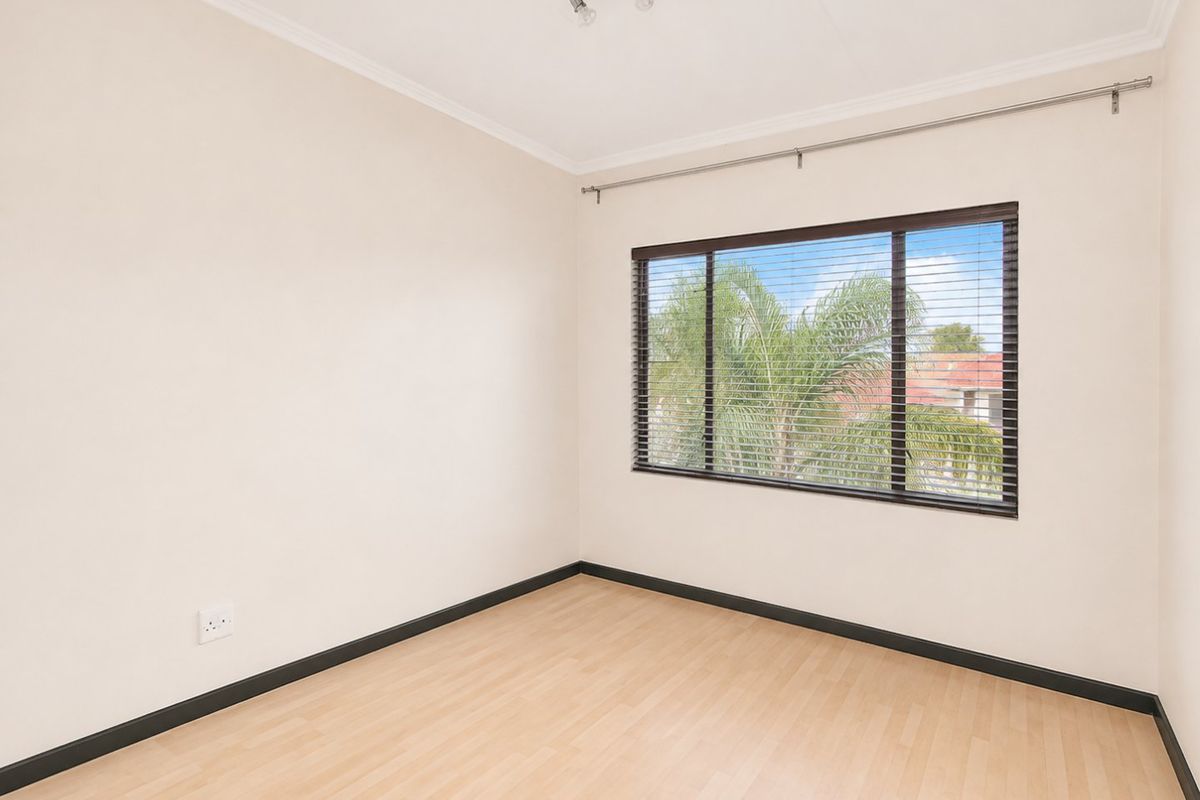 A bright, empty bedroom featuring light laminate flooring, neutral walls, and venetian blinds, offering a clean and versatile space ready for furnishing.