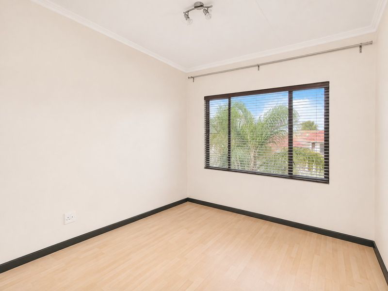 A bright, empty bedroom featuring light laminate flooring, neutral walls, and venetian blinds, offering a clean and versatile space ready for furnishing.