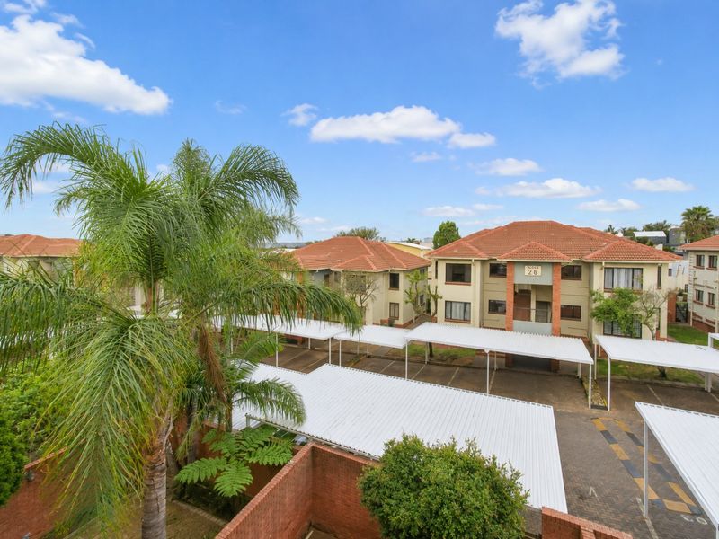 Elevated view of an apartment complex featuring multiple carports, tiled roofing, and paved driveway areas within a residential estate.