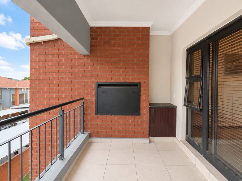 A clean, covered balcony featuring a built-in braai, tiled flooring, and a metal balustrade, offering a functional outdoor space for entertaining.