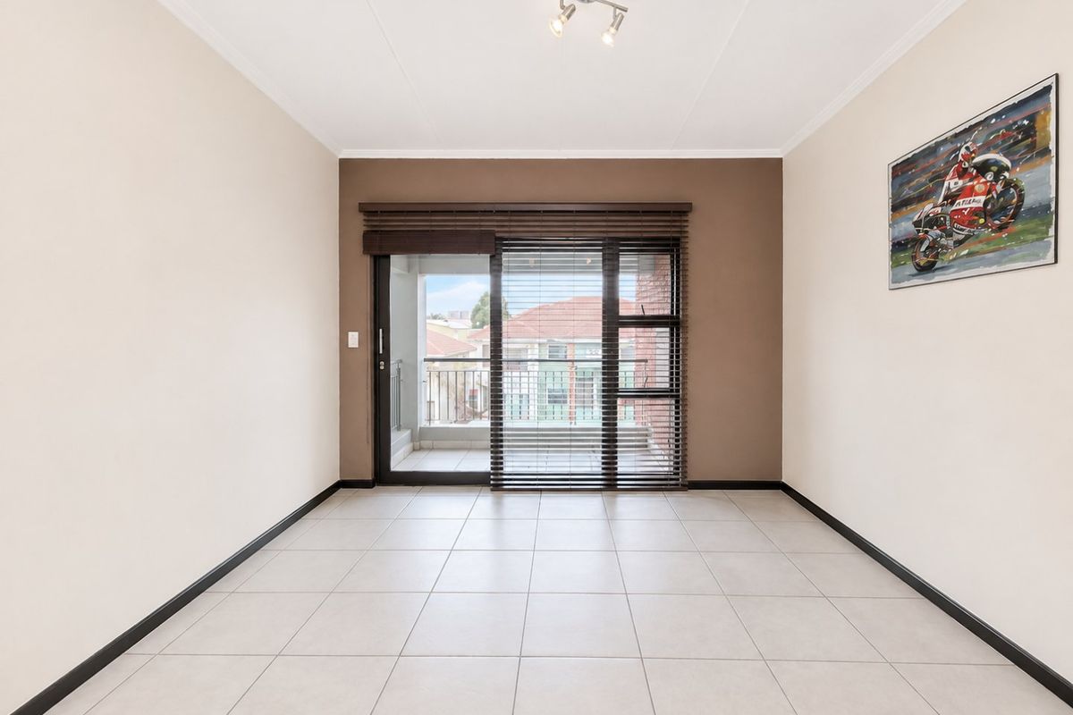 A bright, empty living room featuring neutral tiled flooring, a feature wall, and a sliding glass door providing access to a balcony.