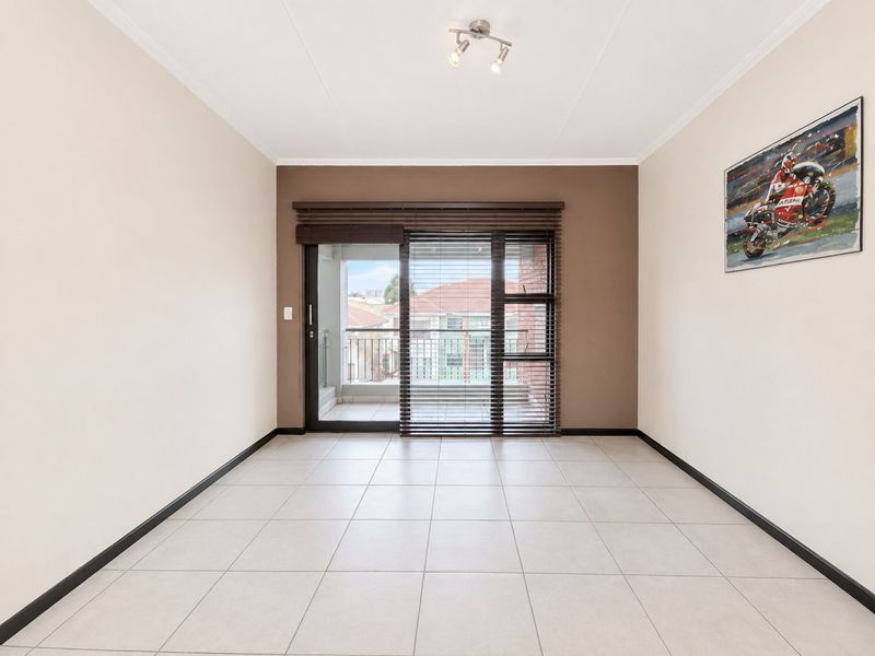A bright, empty living room featuring neutral tiled flooring, a feature wall, and a sliding glass door providing access to a balcony.