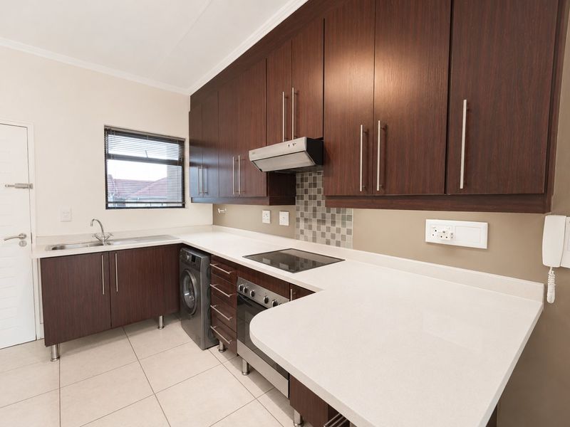 Modern kitchen featuring dark wood cabinetry, stone countertops, integrated electric hob, oven, extractor fan, and tiled flooring with a mosaic backsplash.