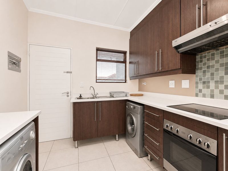 A functional kitchen featuring dark wood cabinetry, white countertops, tiled backsplash, and integrated appliances including an oven, hob, and extractor fan.