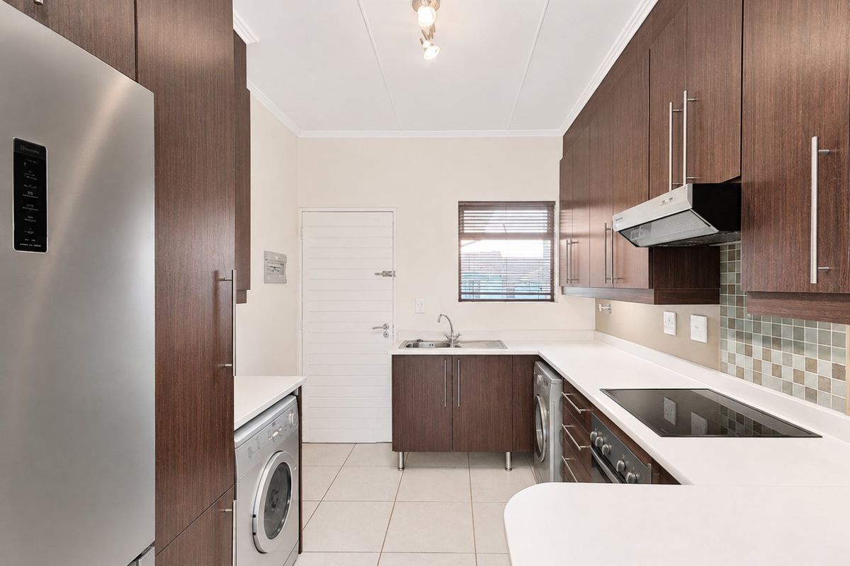 Modern kitchen featuring dark wood cabinetry, white countertops, integrated appliances, tiled backsplash, and functional layout with laundry connection.