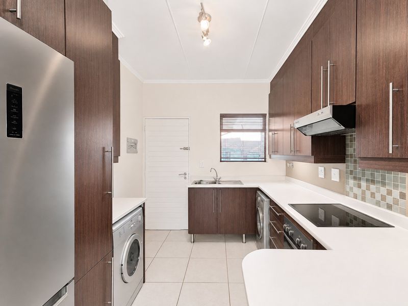 Modern kitchen featuring dark wood cabinetry, white countertops, integrated appliances, tiled backsplash, and functional layout with laundry connection.