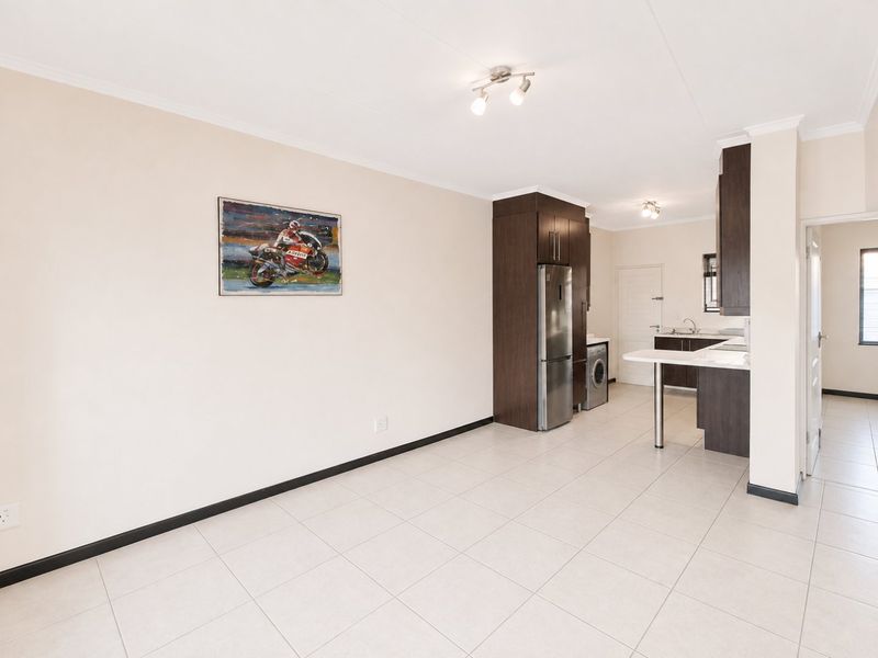 Spacious open-plan living and kitchen area featuring modern dark wood cabinetry, a breakfast bar, and neutral tiled flooring throughout.