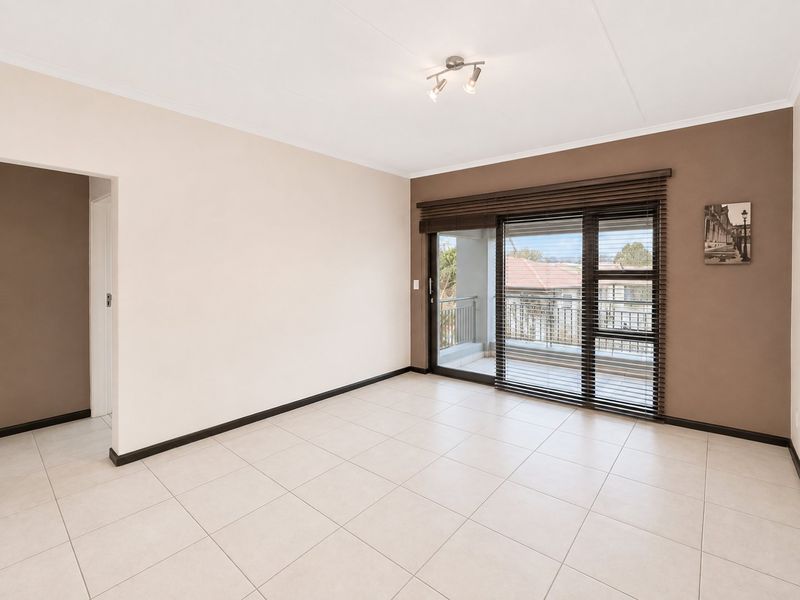 A bright, empty living room featuring neutral tiled flooring, a sliding glass door leading to a balcony, and modern ceiling lighting.