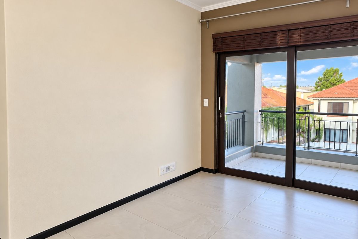 An empty living room featuring neutral tiled flooring, a large sliding glass door leading to a balcony, and clean wall finishes.