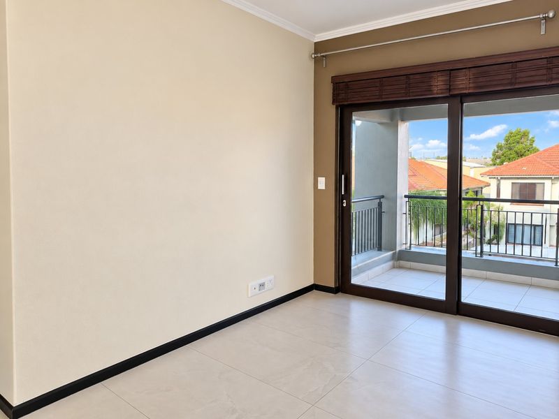An empty living room featuring neutral tiled flooring, a large sliding glass door leading to a balcony, and clean wall finishes.