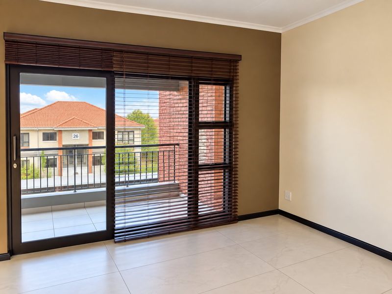 A bright, empty living area featuring large sliding glass doors with wooden blinds, neutral wall tones, and clean tiled flooring leading to a balcony.