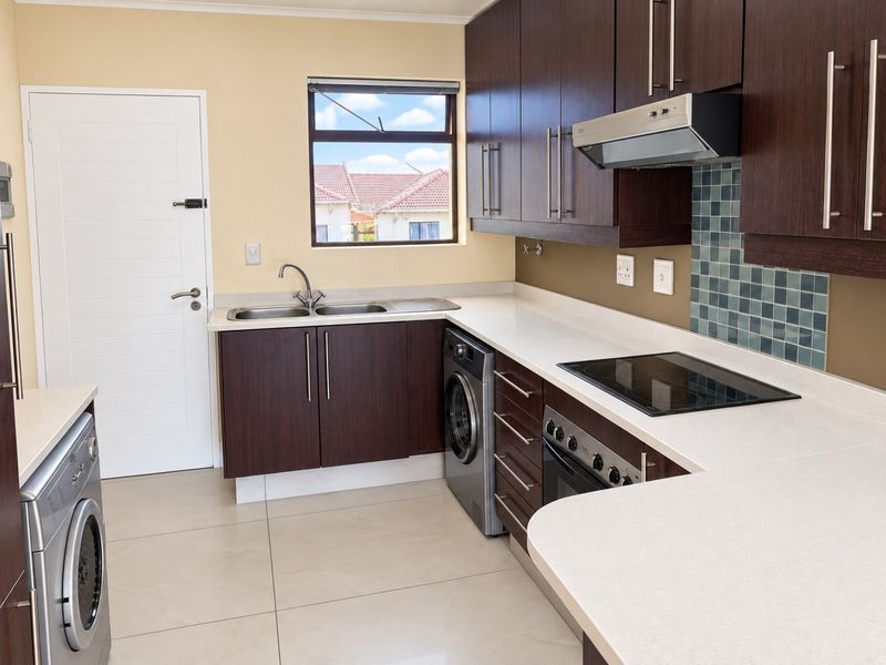 A modern kitchen featuring dark wood cabinetry, white stone countertops, integrated appliances, and tiled flooring, offering a clean and functional workspace.