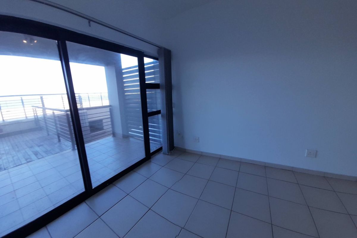 An empty living room featuring tiled flooring and a large sliding glass door providing access to an outdoor balcony area.