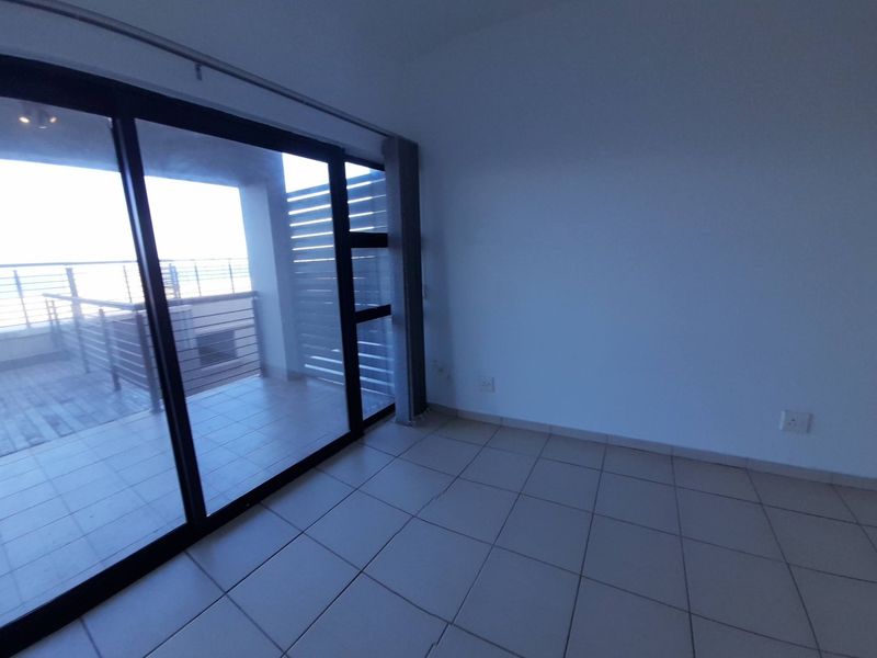 An empty living room featuring tiled flooring and a large sliding glass door providing access to an outdoor balcony area.