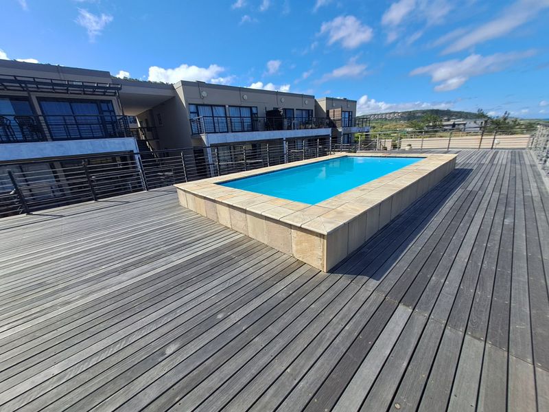 A rooftop swimming pool area featuring timber decking, stone coping, and metal balustrades, set against a modern apartment building exterior.