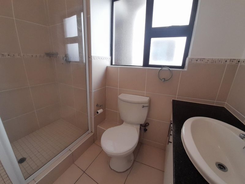 A clean, functional bathroom featuring a glass-enclosed shower, a vanity with a granite countertop, and neutral floor-to-ceiling wall tiles.