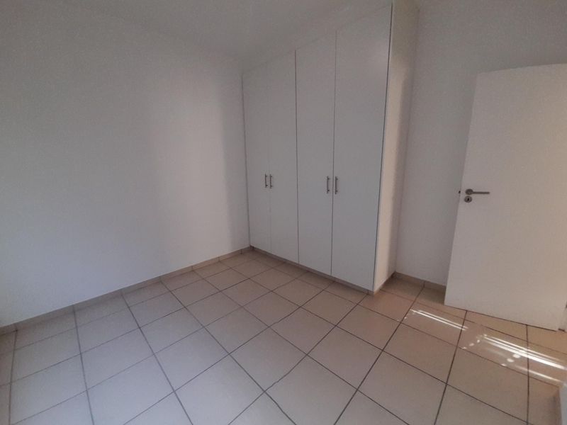 A clean, empty bedroom featuring neutral tiled flooring and white built-in cupboards, offering a blank canvas for personalization.