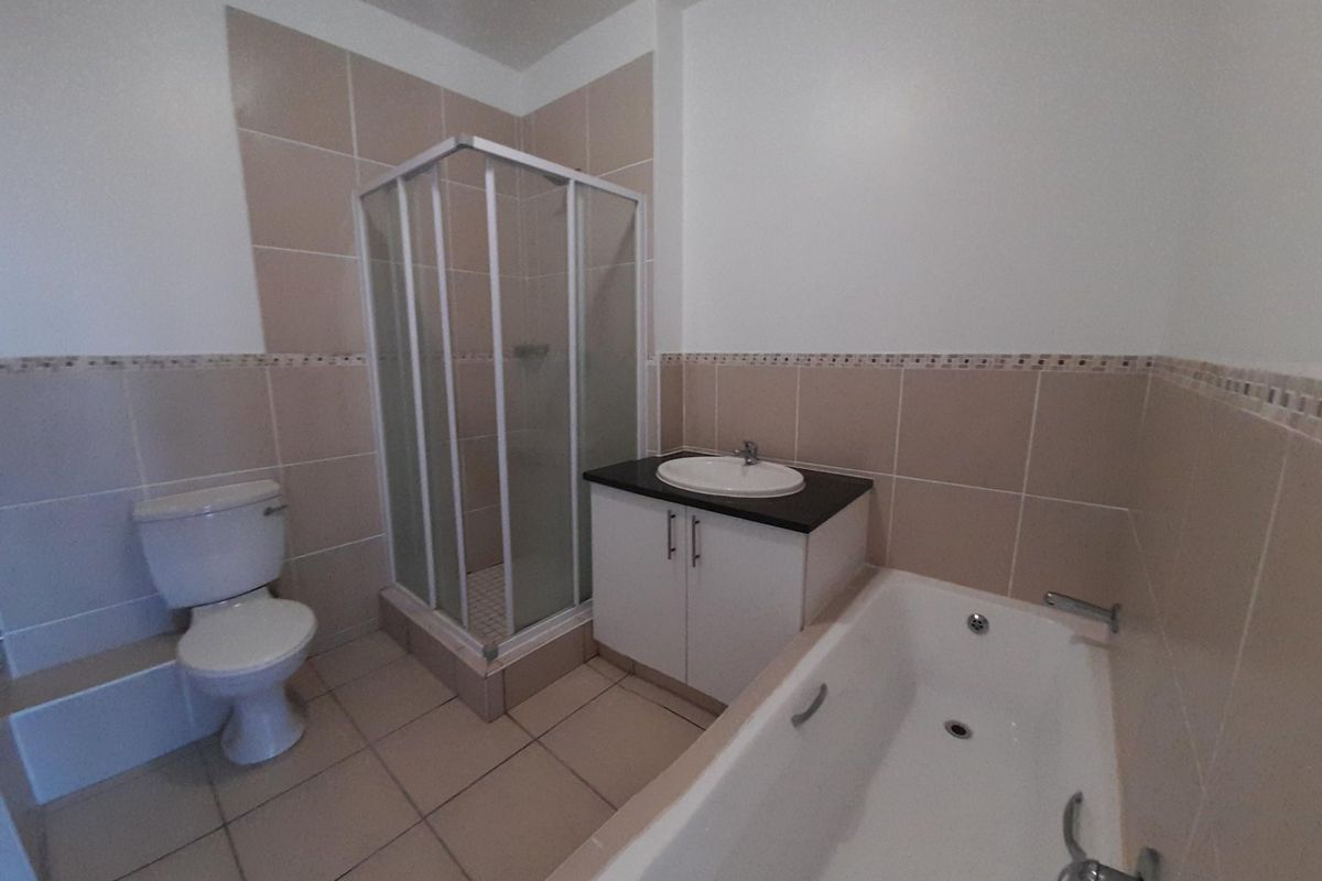 A clean, functional bathroom featuring a separate shower enclosure, bathtub, vanity unit with basin, and toilet, finished with neutral wall and floor tiling.