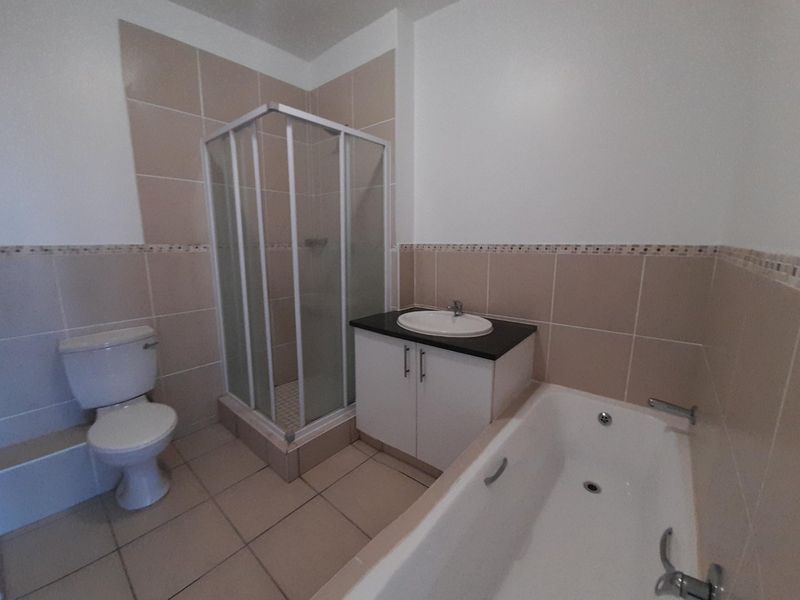 A clean, functional bathroom featuring a separate shower enclosure, bathtub, vanity unit with basin, and toilet, finished with neutral wall and floor tiling.