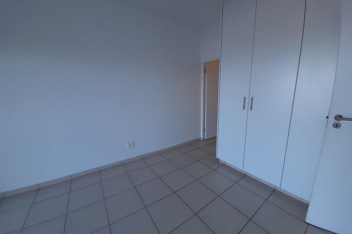 An empty bedroom featuring neutral tiled flooring and white built-in cupboards, offering a clean and versatile space ready for personalization.