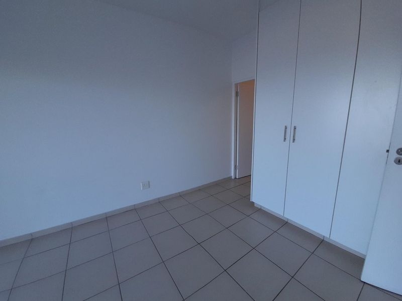 An empty bedroom featuring neutral tiled flooring and white built-in cupboards, offering a clean and versatile space ready for personalization.