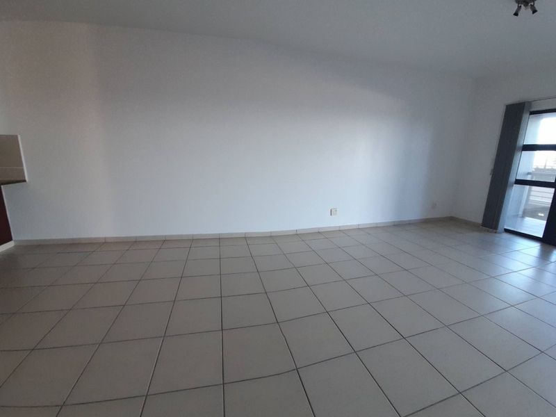 An empty open-plan living area featuring neutral tiled flooring and a sliding glass door leading to an outdoor space.