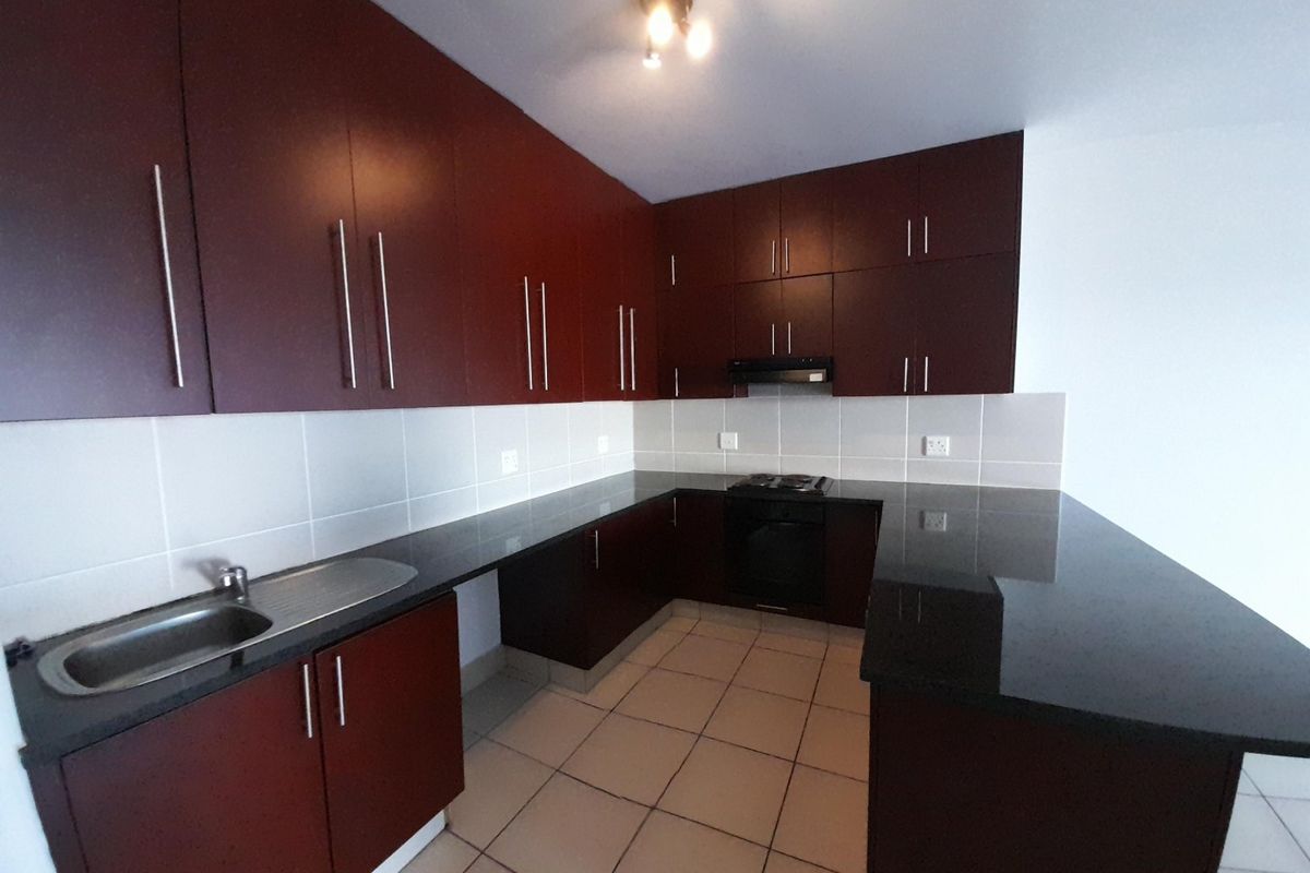 A clean, empty kitchen featuring dark wood cabinetry, granite countertops, built-in oven, hob, and extractor fan with neutral tiled flooring and backsplash.