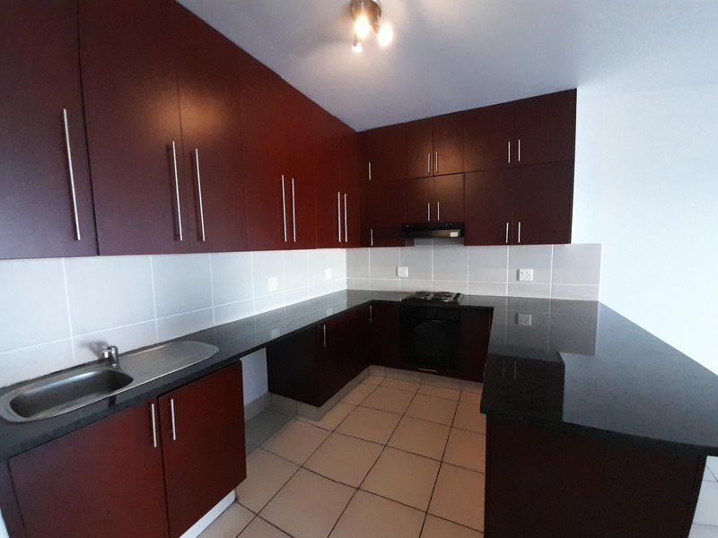 A clean, empty kitchen featuring dark wood cabinetry, granite countertops, built-in oven, hob, and extractor fan with neutral tiled flooring and backsplash.