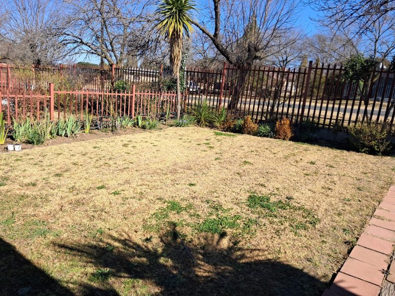 A private rear garden area featuring a lawn, established perimeter metal fencing, and a paved border.