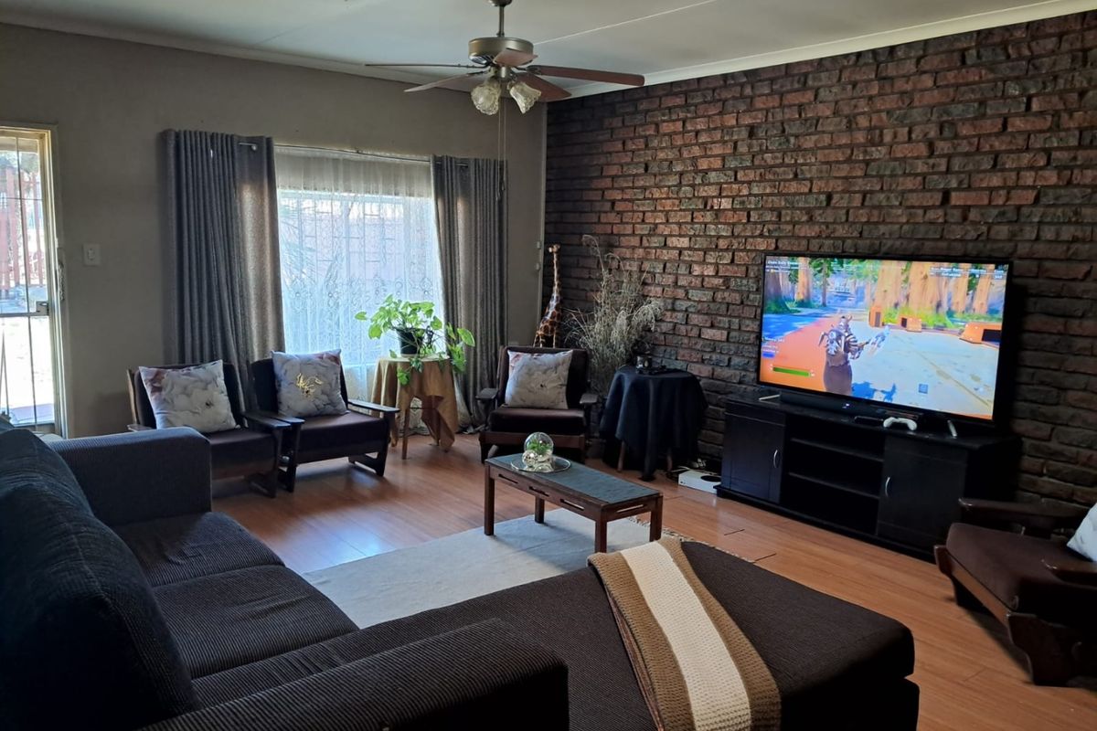 A comfortable living room featuring a prominent exposed brick wall, laminate flooring, and a ceiling fan, providing a warm and textured living space.