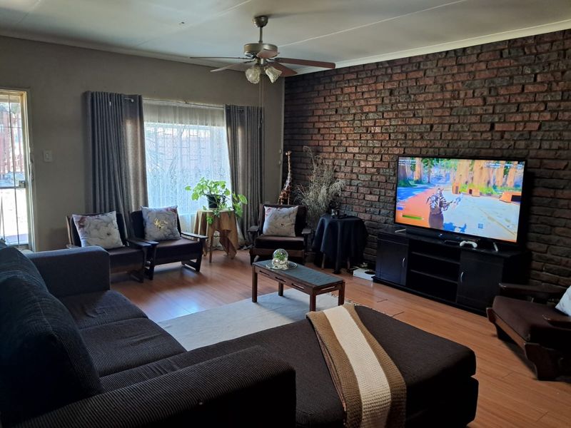 A comfortable living room featuring a prominent exposed brick wall, laminate flooring, and a ceiling fan, providing a warm and textured living space.