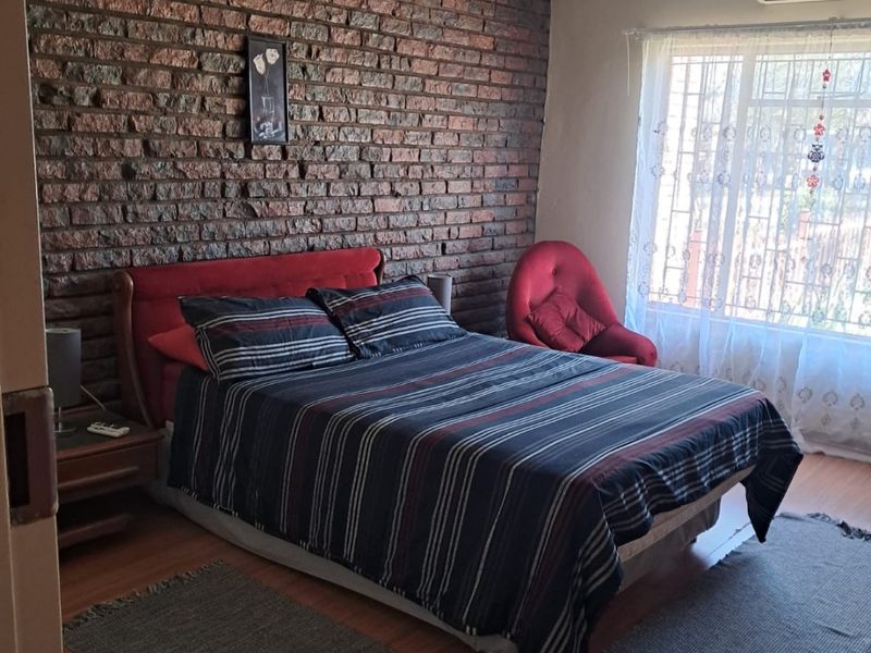 A bedroom featuring an exposed brick wall, laminate flooring, a ceiling fan, and a wall-mounted air conditioning unit.