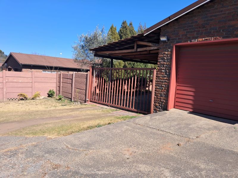 Front exterior view of the property featuring a brick facade, attached garage, carport, and a concrete driveway with perimeter walling.