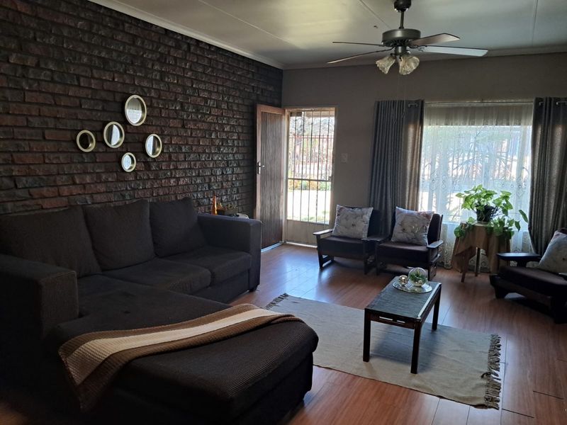 A living room featuring an exposed brick accent wall, laminate flooring, and a ceiling fan, with direct access to an exterior security gate.