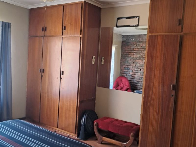 Bedroom featuring extensive built-in wooden cabinetry, laminate flooring, and a ceiling fan, offering ample storage space with a dated aesthetic.